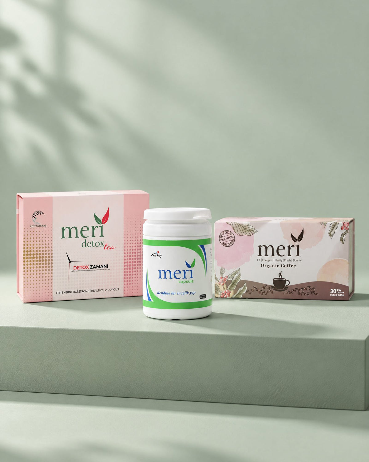 Meri Detox Tea, Meri Capsule and Meri Organic Coffee standing side by side on a sage plinth