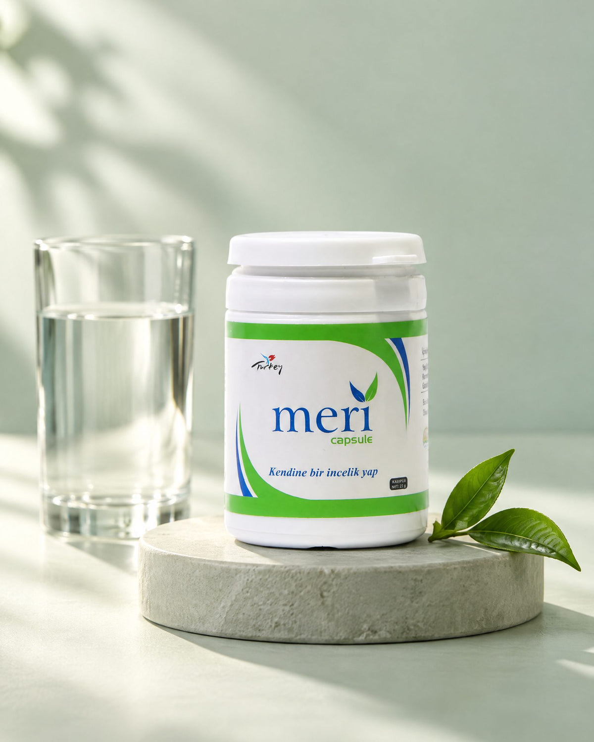 Detox-Kapseldose auf einem salbeifarbenen Sockel neben einem Glas Wasser